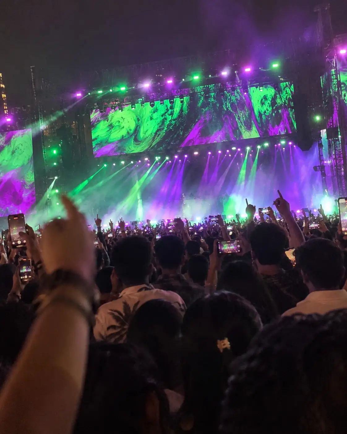 Illustration: a phone photo from inside a concert crowd, raised hands and phones in front of a stage with swirling green and purple visuals