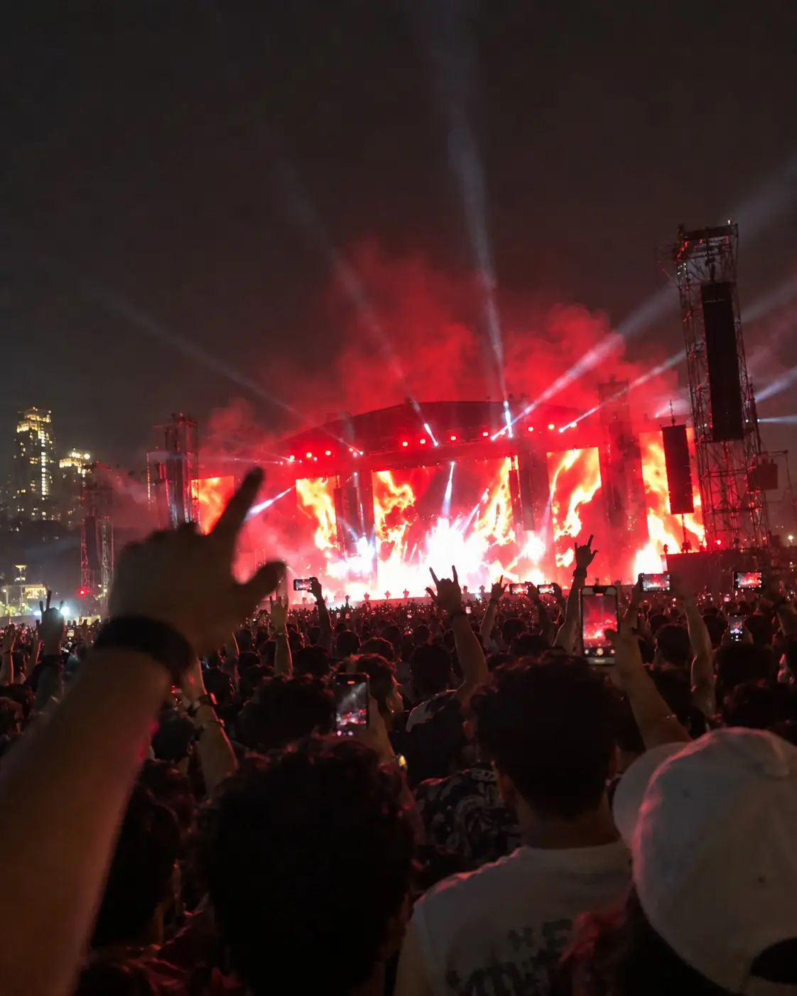 Illustration: a phone photo from inside a night crowd, a raised fist in front of a red-lit stage with smoke and city towers
