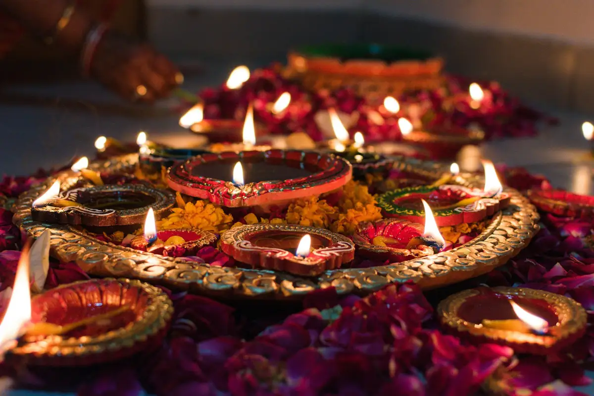Lit clay diyas and candles on a decorated tray with flower petals
