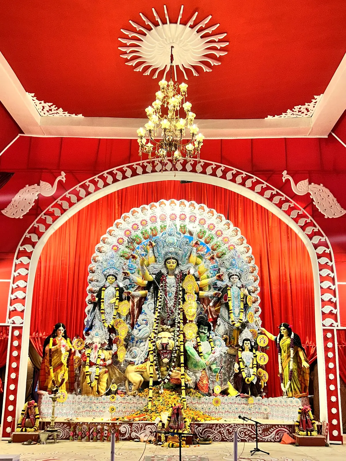 The Durga idol with her family under a red canopy in a lit pandal