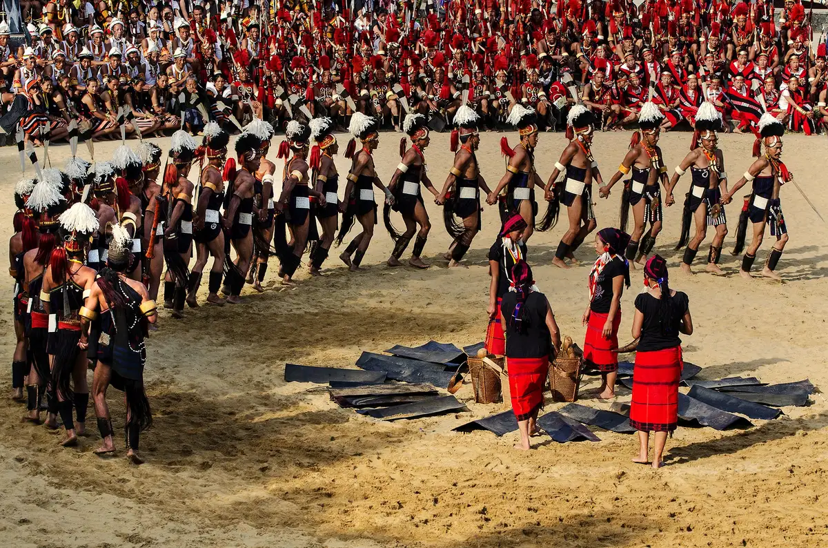 Naga warriors in feathered headgear dancing in a circle in the Hornbill Festival arena