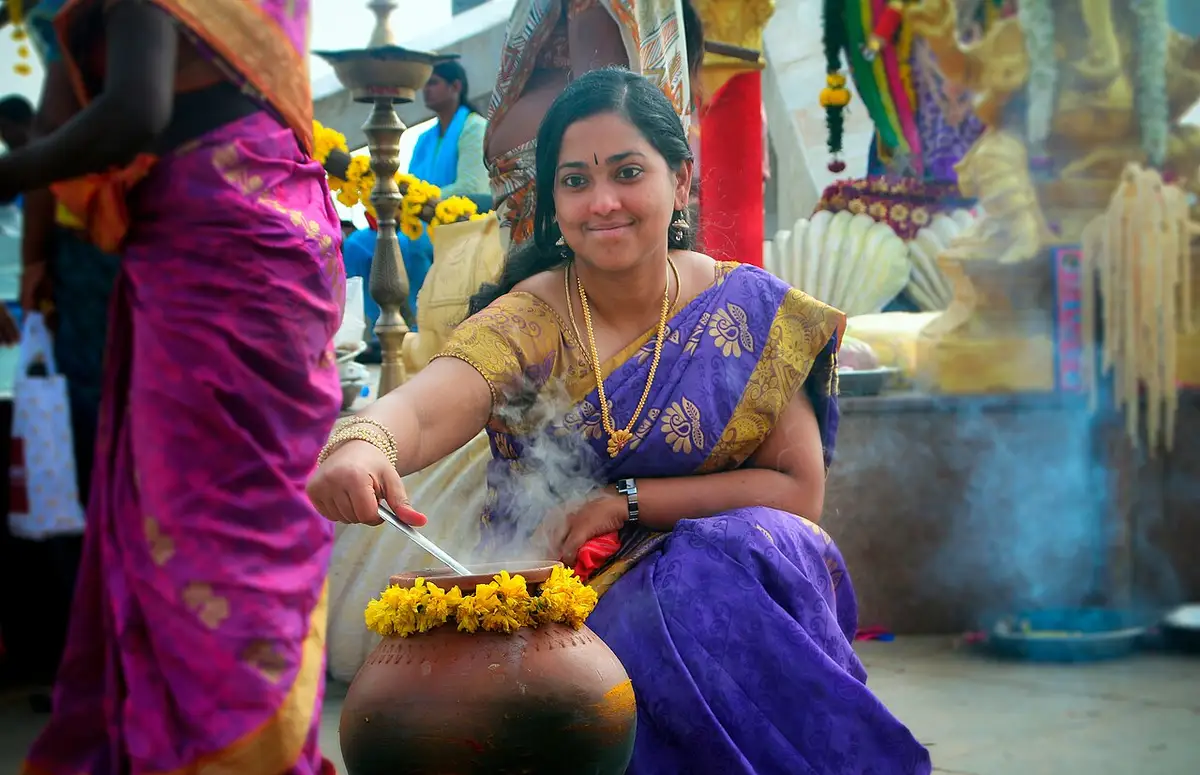 A woman in a silk sari stirring pongal in a decorated pot
